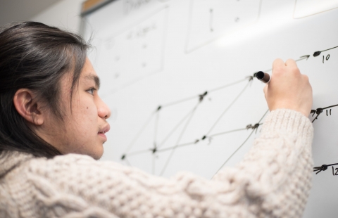 A photo of a male student doing math equations on a whiteboard