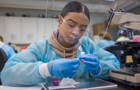 Student with face shield looks at microscope slide