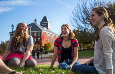 Three female college students sit outside on the lawn in fall