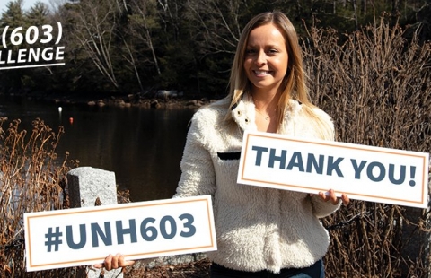 Female college student holding signs that read UNH603 and Thank You