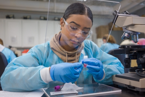 Student with face shield looks at microscope slide