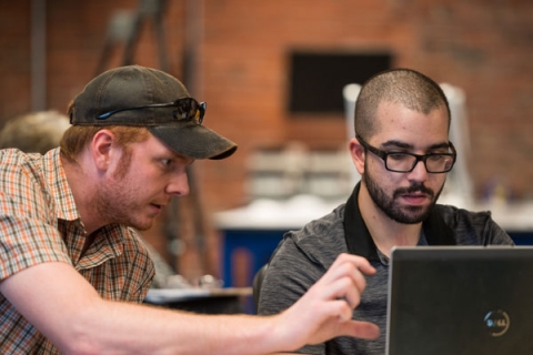 UNH Manchester professor Mihaela Sabin works with a student using a laptop.