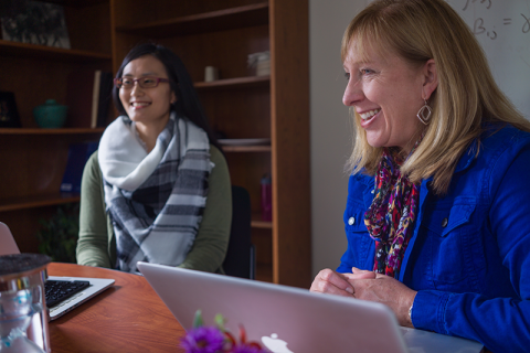 two women smiling and working on laptops