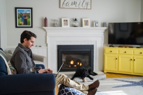 College student sitting in front of a fireplace looking at his laptop